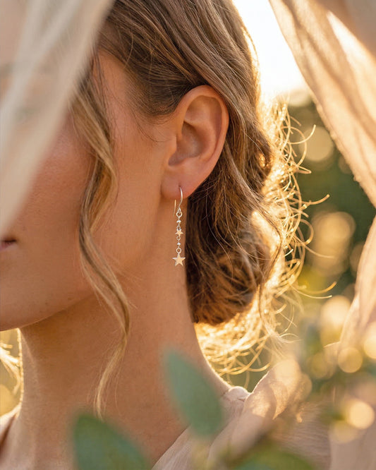 Close-up of a person wearing silver star earrings with a blurred natural background