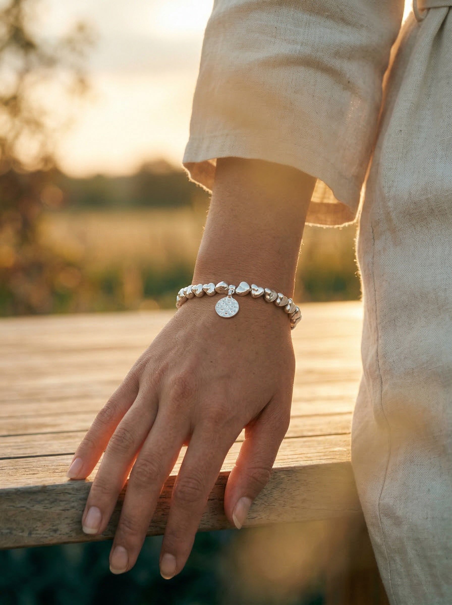 Person wearing a bracelet with a hammered disc charm on a wooden surface with a blurred natural background