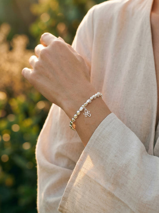 Close-up of a person wearing a silver flower bracelet with a blurred natural background