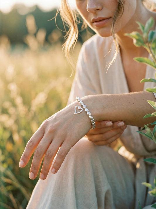 Woman wearing a silver bracelet with heart charm in a natural setting at golden hour