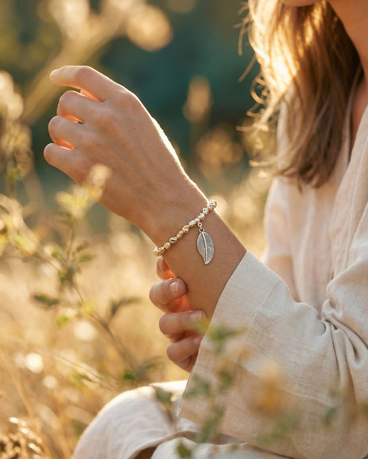 Woman wearing a silver bracelet with a leaf charm in a natural setting