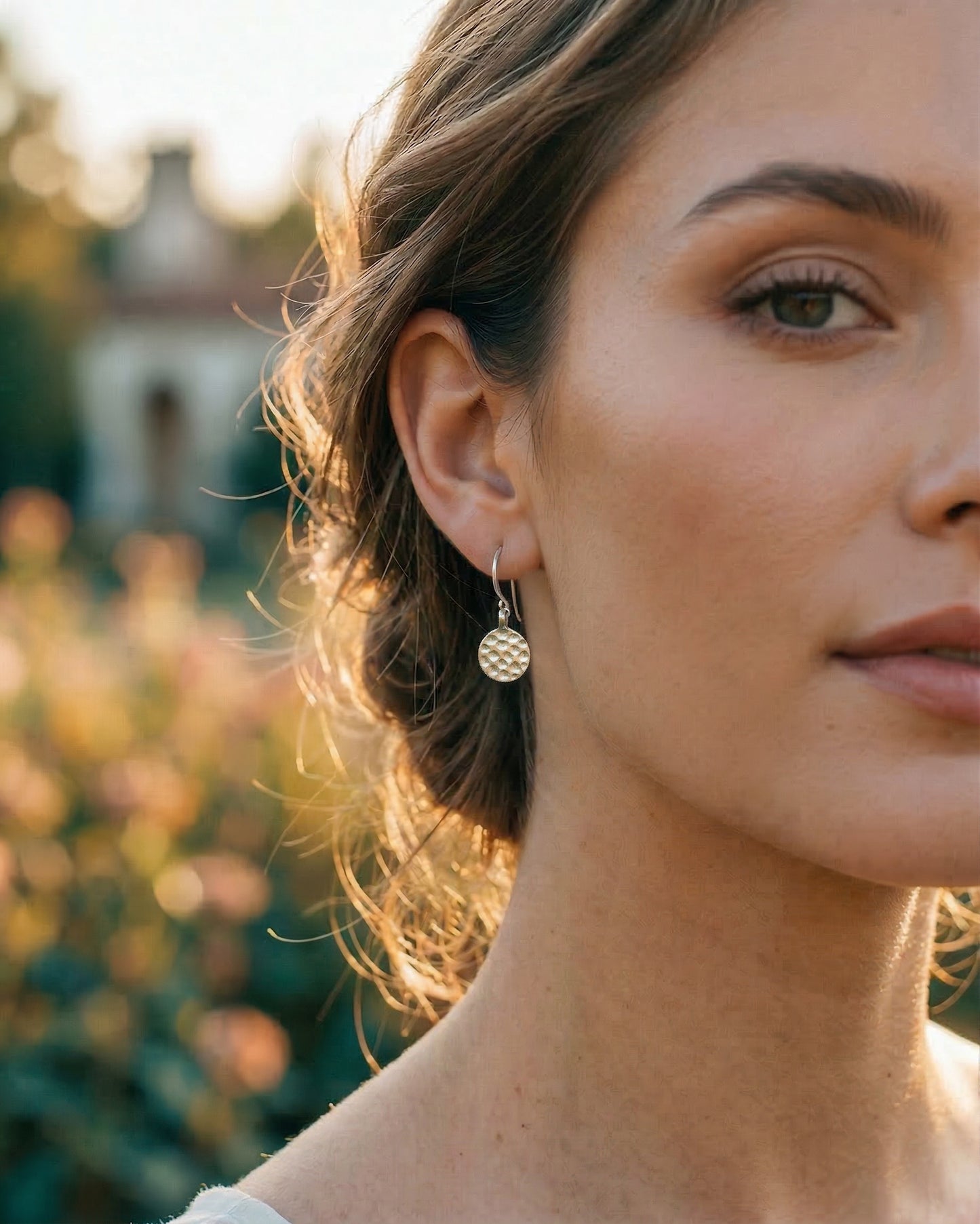 Close-up of a woman wearing a silver disc earring with a blurred outdoor background