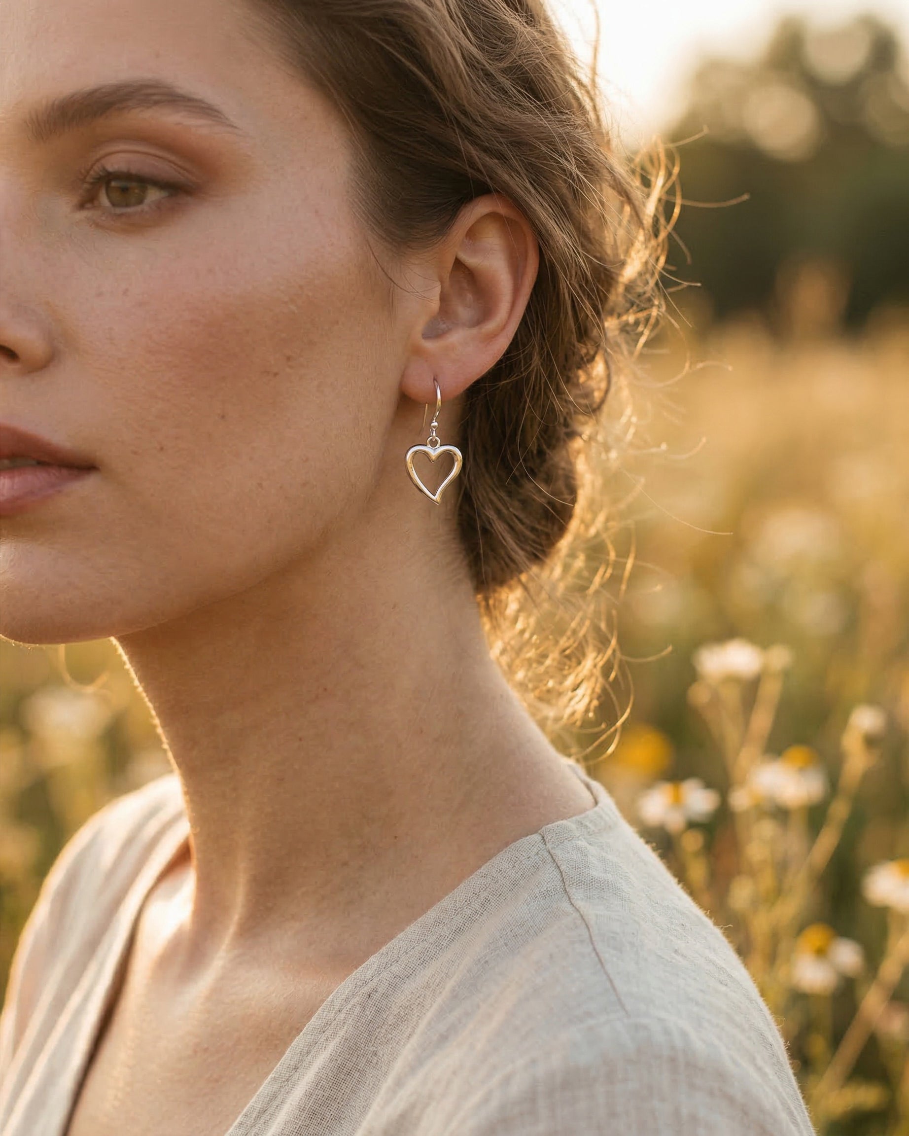 Woman wearing heart-shaped silver charmearrings in a natural setting with blurred background