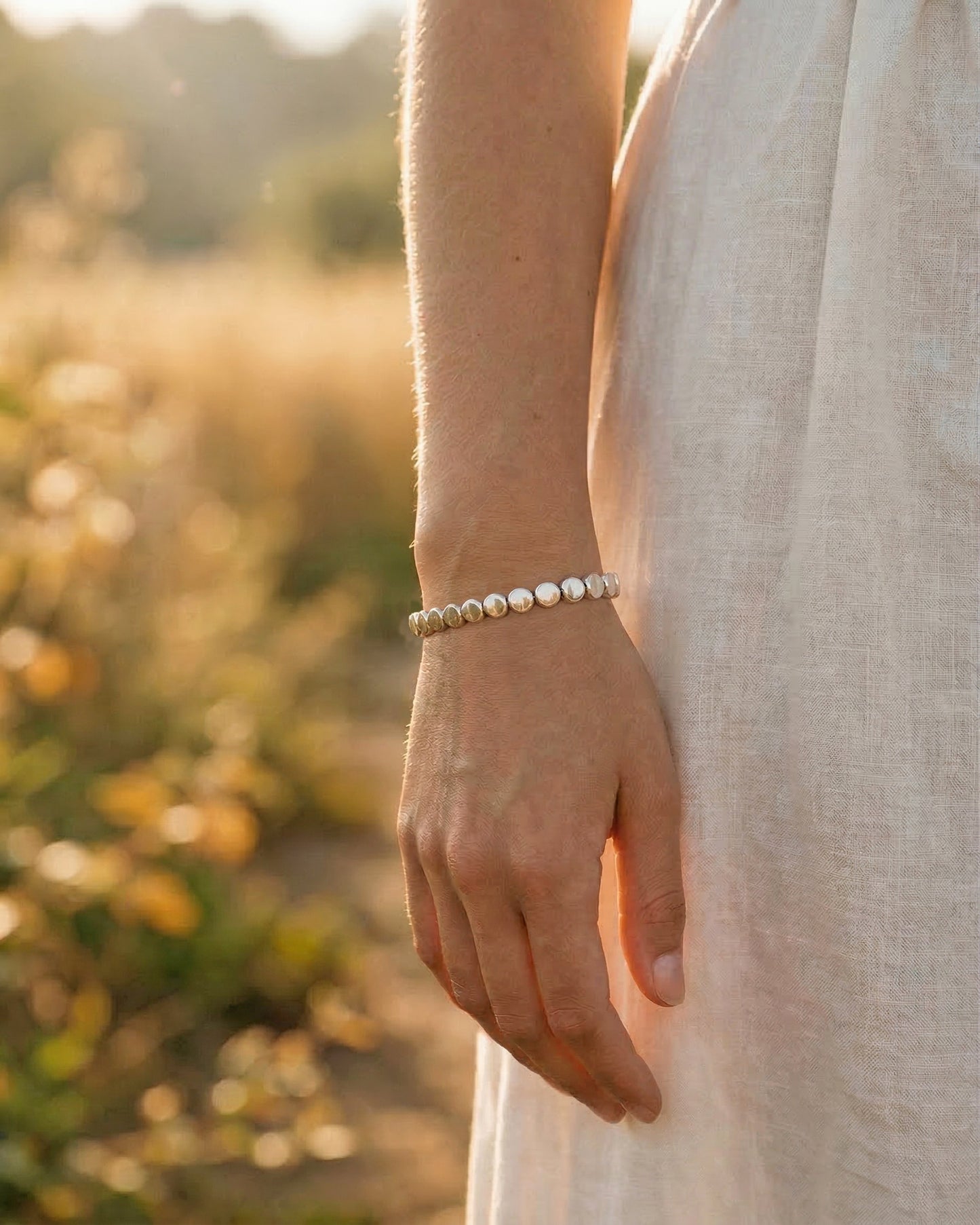 Woman wearing a silver disc bracelet in a natural setting at golden hour with blurred background