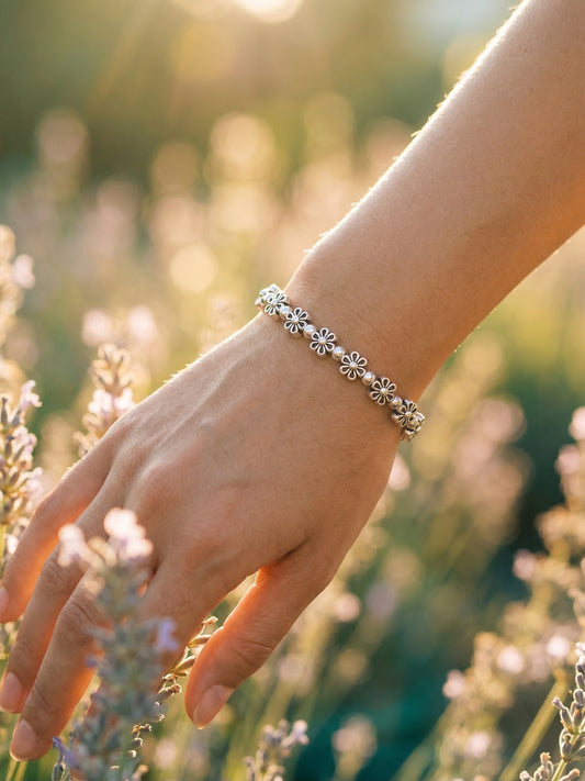 Hand wearing a silver bracelet with floral beads against a blurred natural background