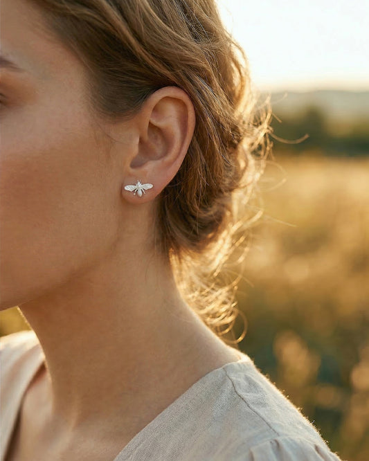 Close-up of a person wearing silver bee earrings with a blurred natural background