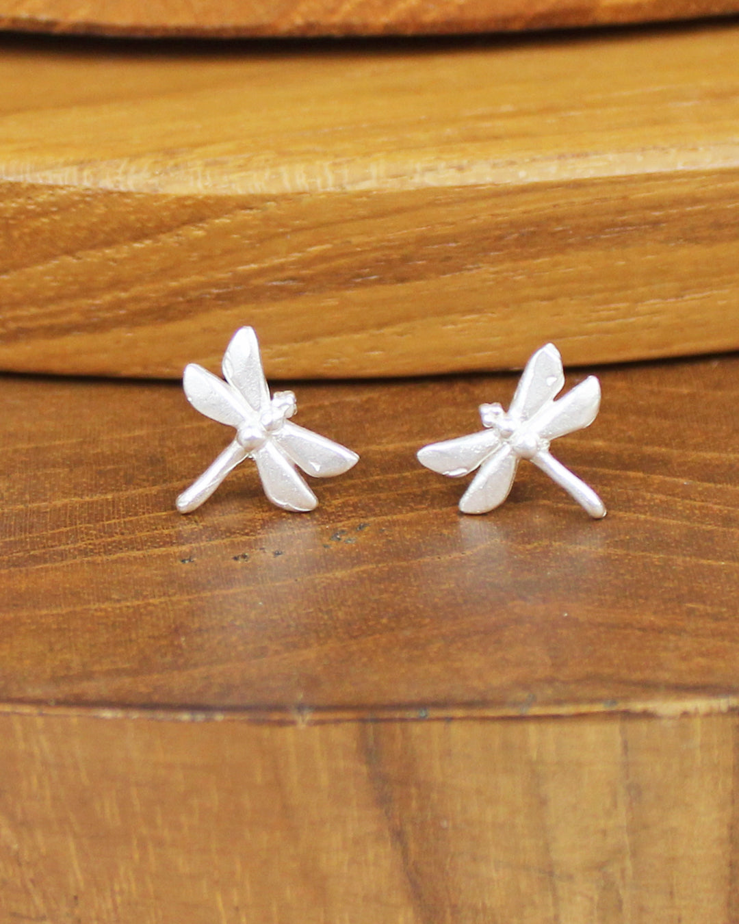 Silver dragonfly shaped earrings on a wooden background