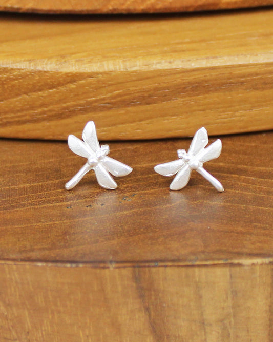 Silver dragonfly shaped earrings on a wooden background