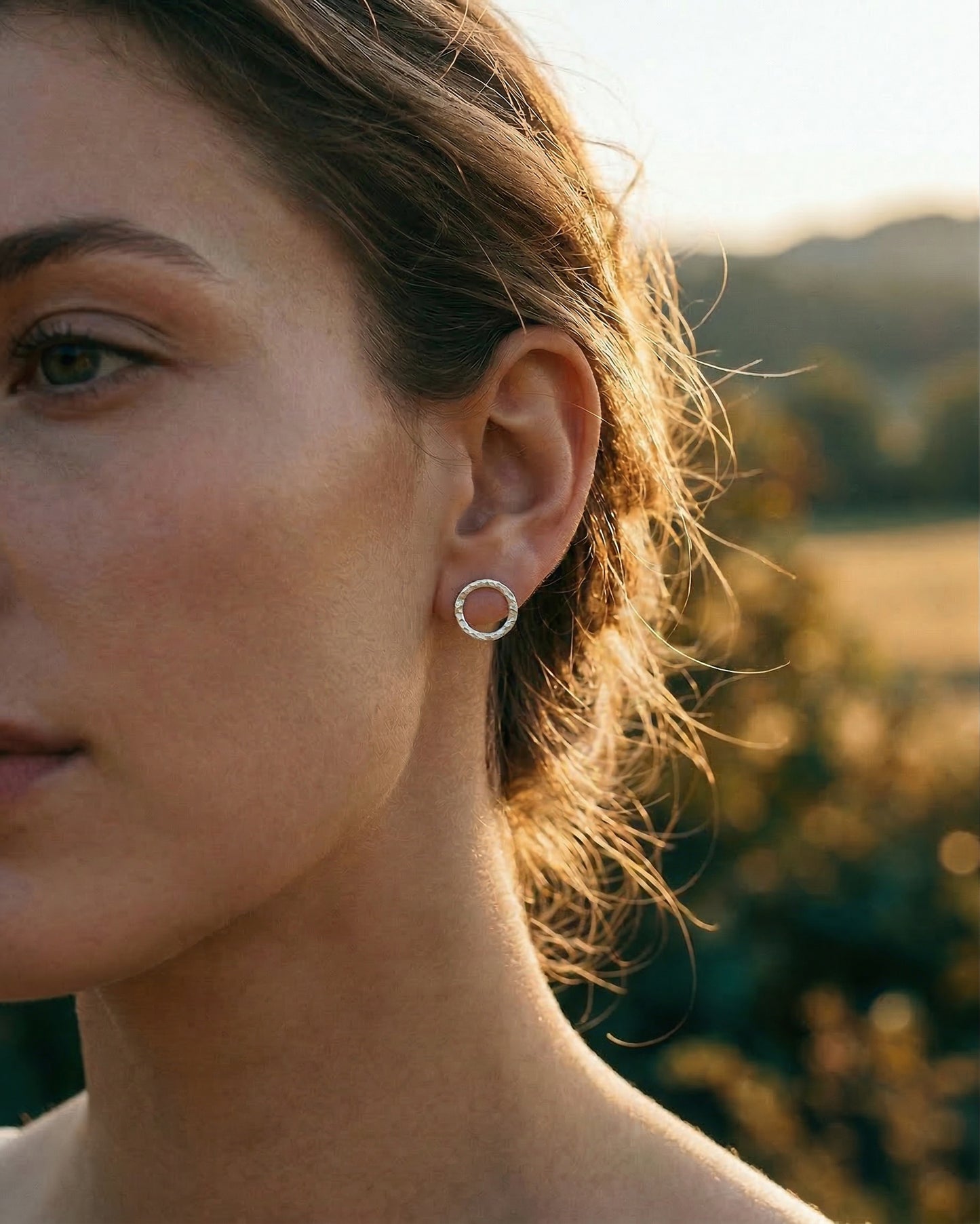 Close-up of a person wearing silver hoop earrings with a blurred natural background
