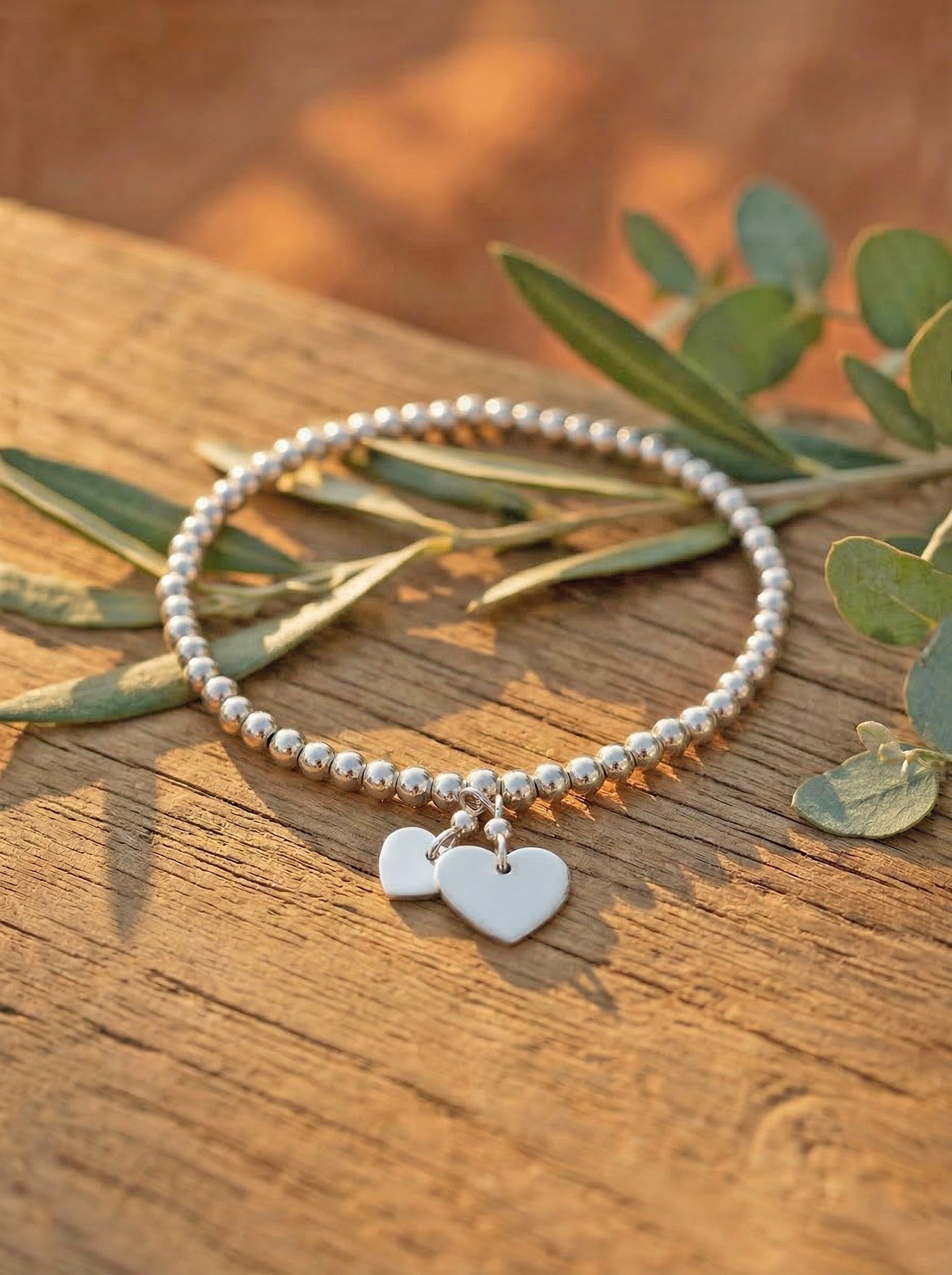silver bracelet with heart charms on a wooden surface with leaves