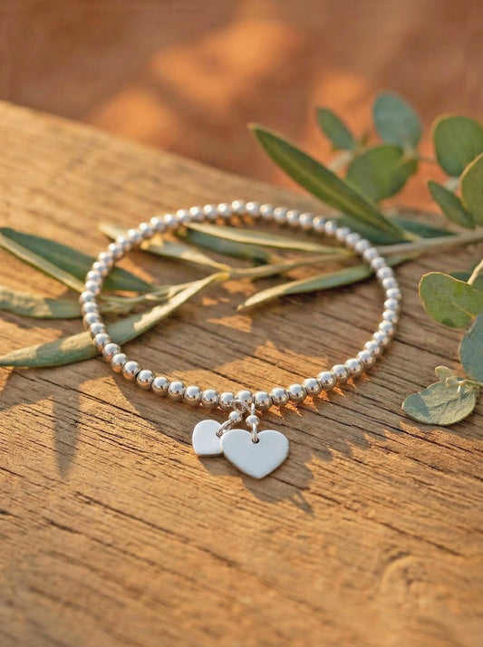 silver bracelet with heart charms on a wooden surface with leaves
