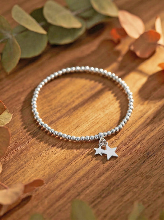 Silver beaded bracelet with a star charm on a wooden surface with leaves.