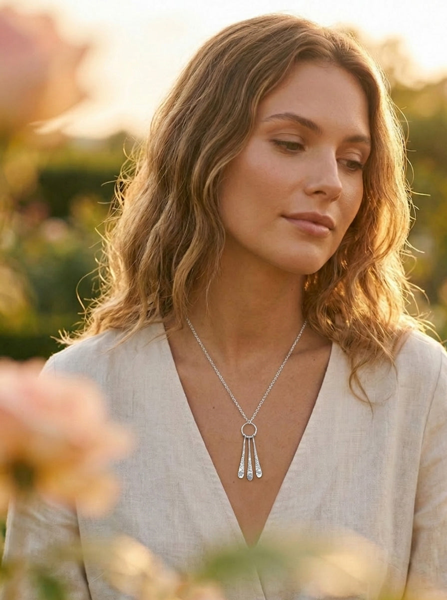 Woman wearing a silver necklace with a pendant in a natural setting at golden hour