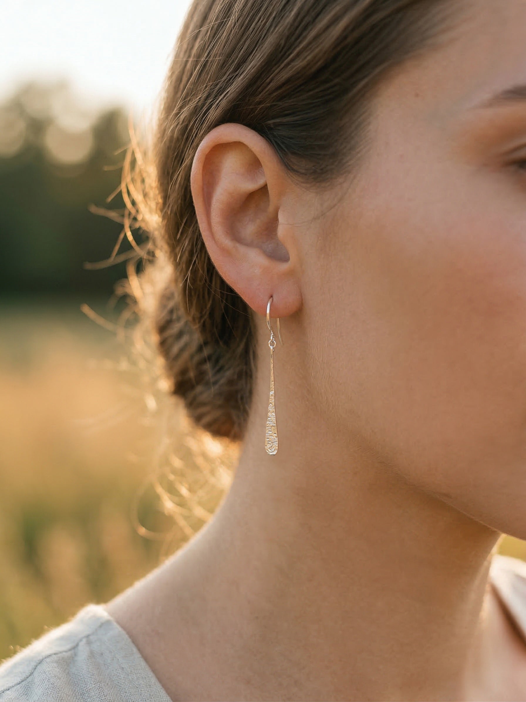 Close-up of a person wearing silver teardrop earrings with a blurred natural background