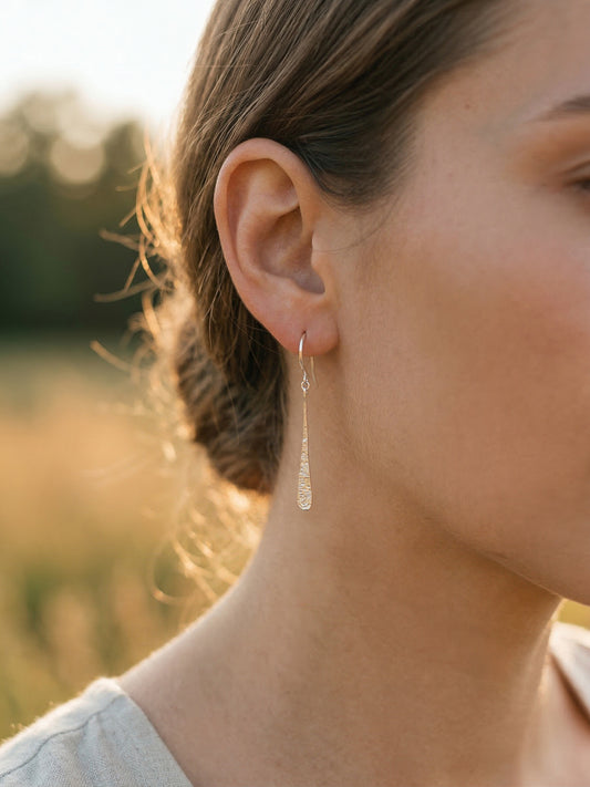 Close-up of a person wearing silver teardrop earrings with a blurred natural background