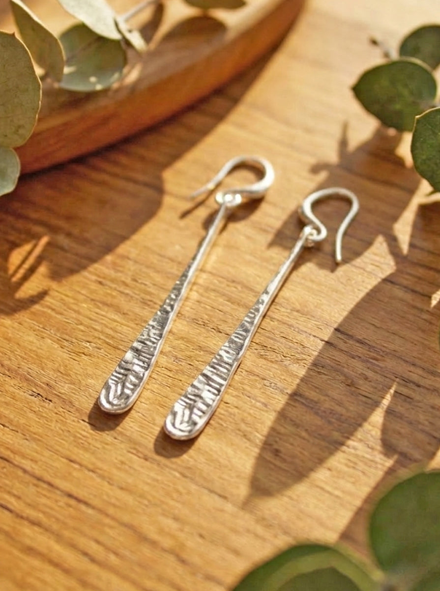 Silver teardrop earrings on a wooden surface with green leaves
