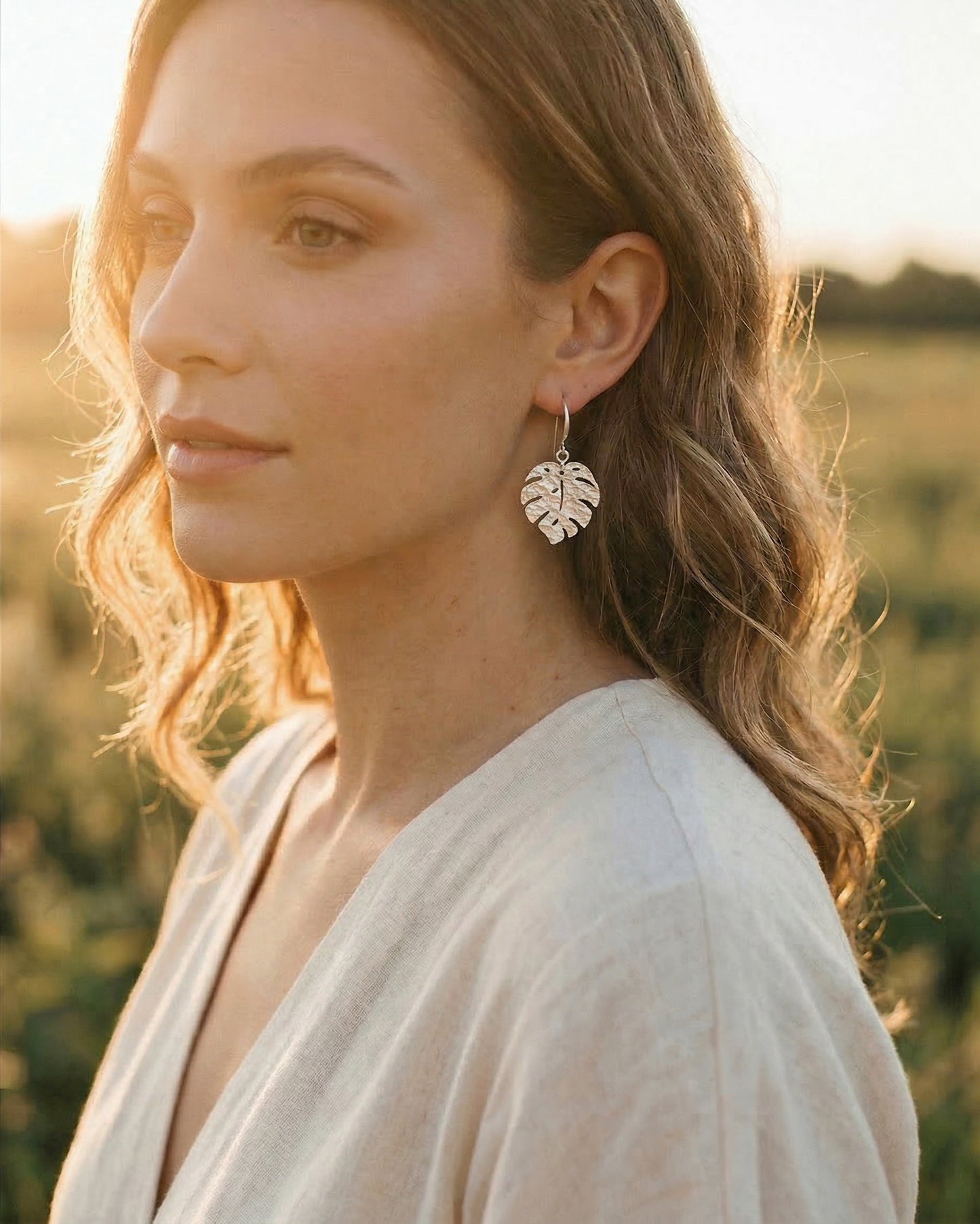 Woman wearing silver monstera leaf earrings in a natural setting