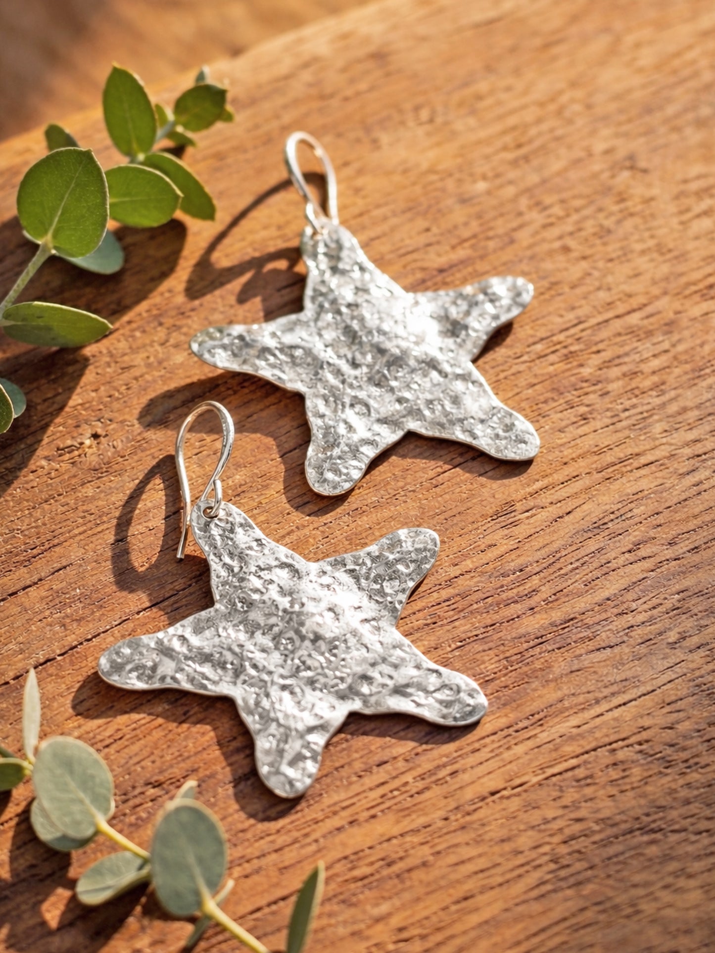 Star-shaped silver earrings on a wooden surface with green leaves.