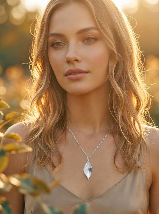 Woman wearing a silver necklace with a leaf pendant in a natural setting at golden hour