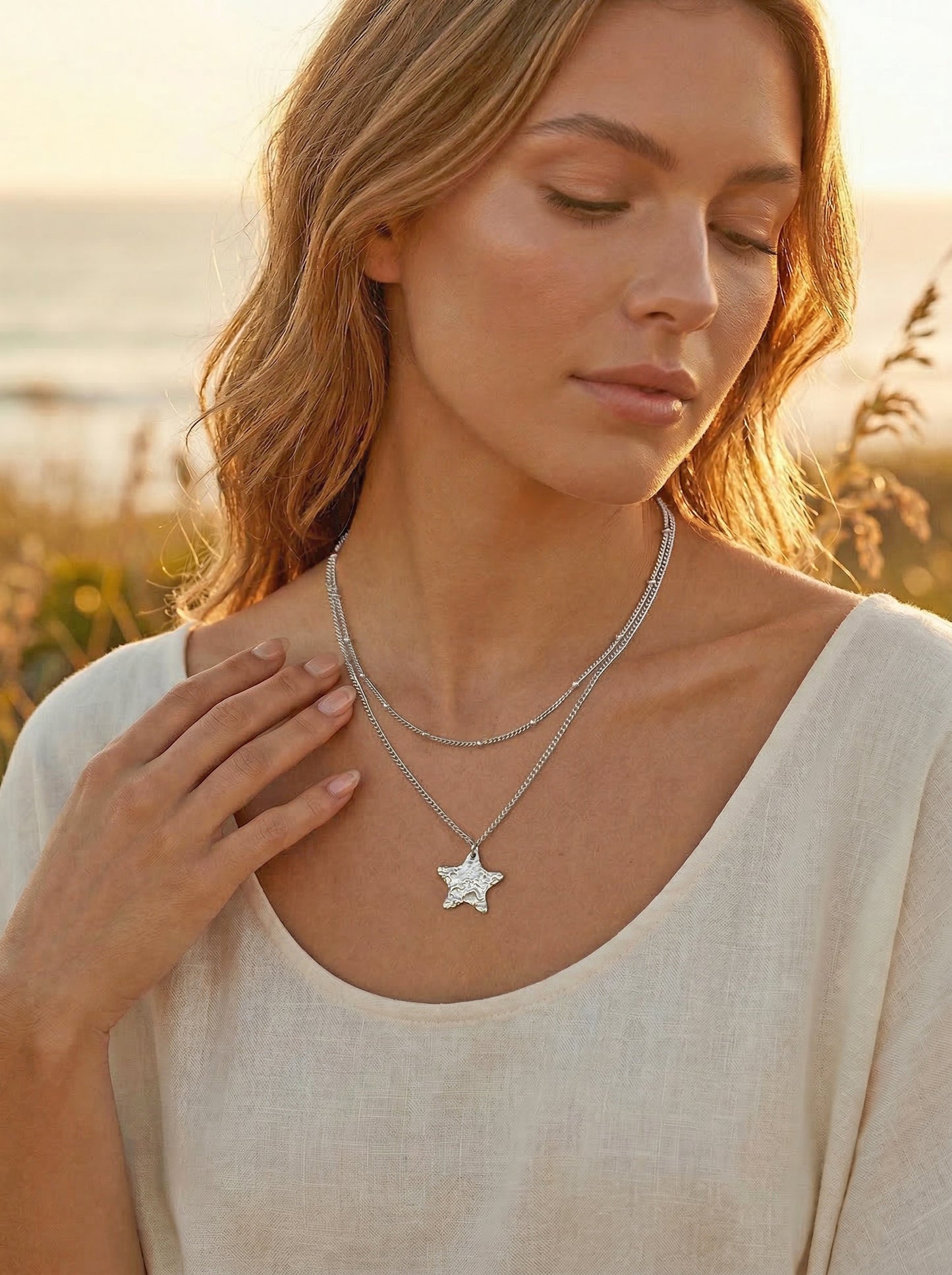 Woman wearing a silver star-shaped necklace with a blurred natural golden hour background