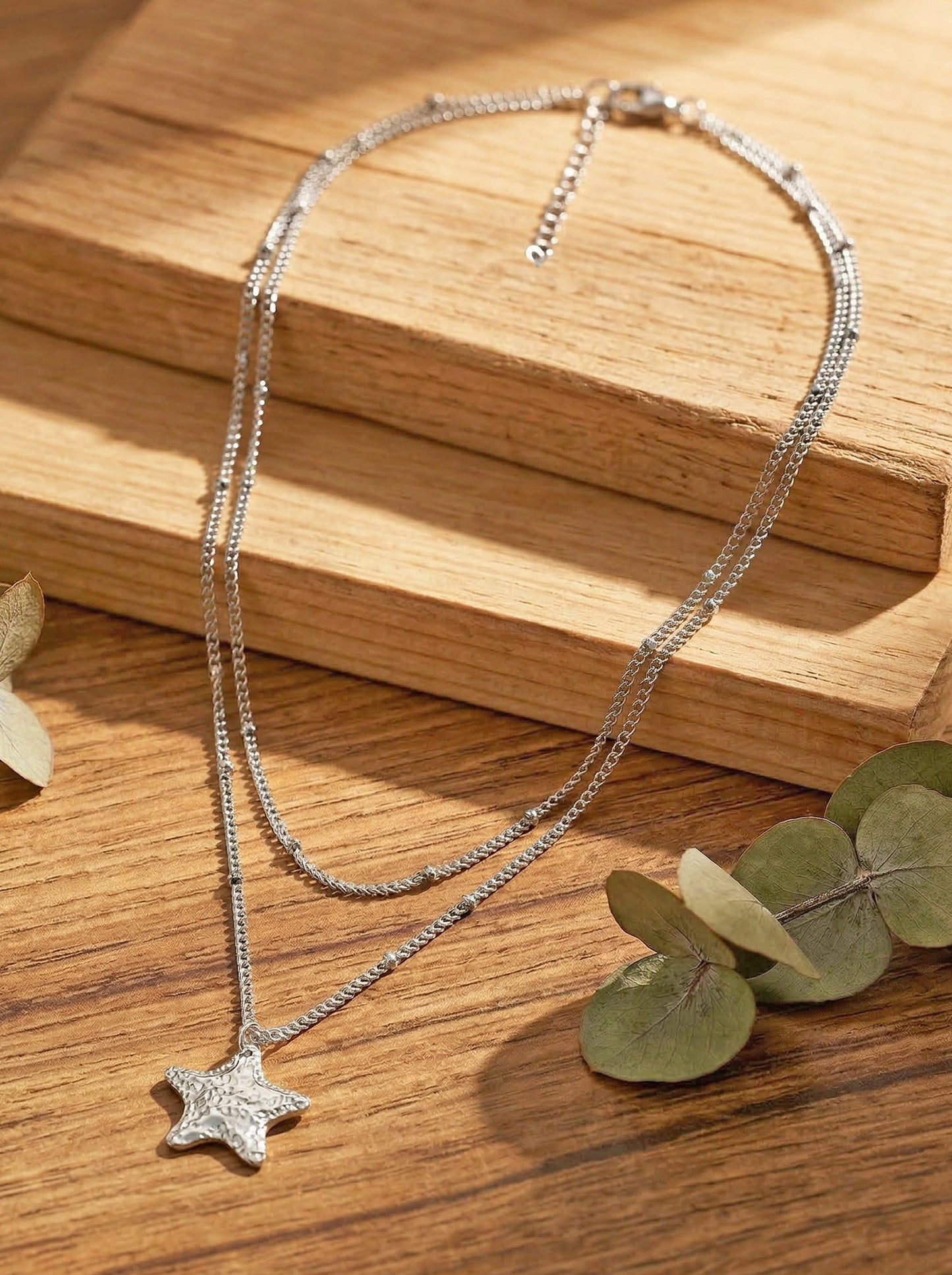 Silver-plated star necklace on a wooden surface with eucalyptus leaves