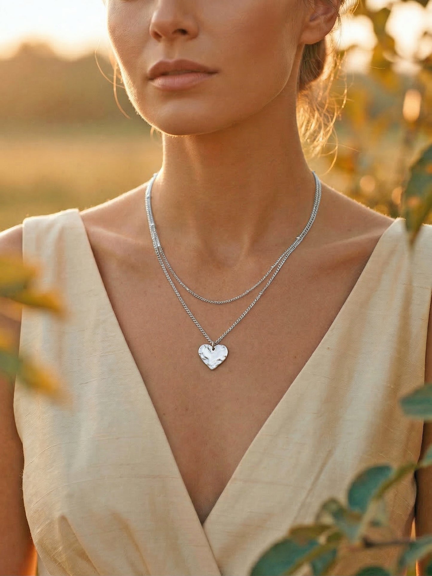 Woman wearing a silver-plated necklace with a heart pendant in a golden hour natural setting