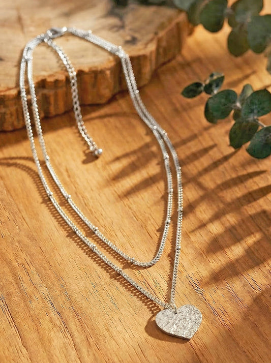Silver-plated necklace with a hammered heart pendant on a wooden surface