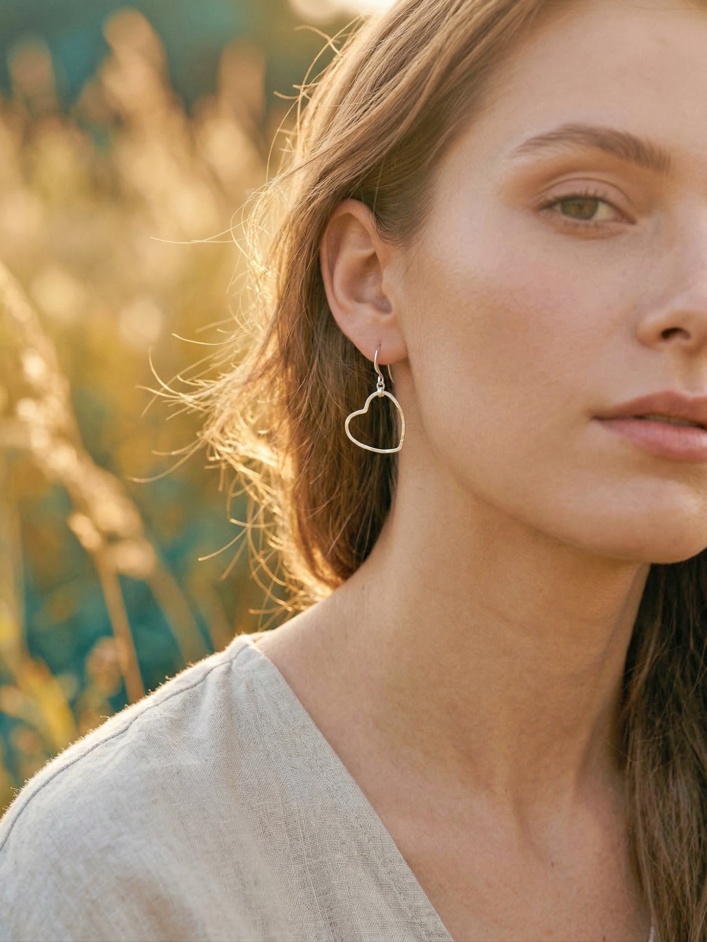 Woman wearing a silver heart-shaped earring with a blurred natural background