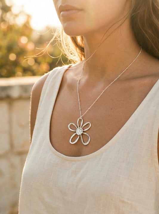 Woman wearing a large silver flower-shaped necklace outdoors