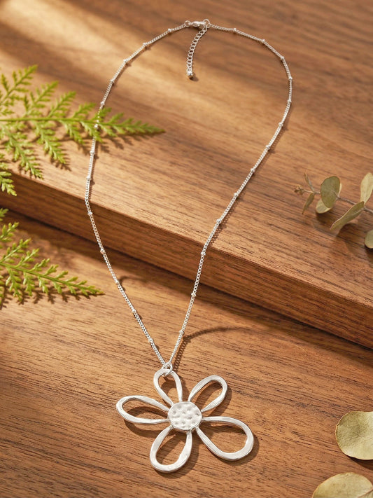 Silver flower pendant necklace on a wooden surface with green leaves.