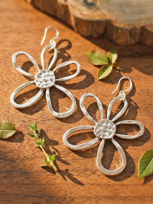 Silver flower-shaped earrings on a wooden surface with leaves.