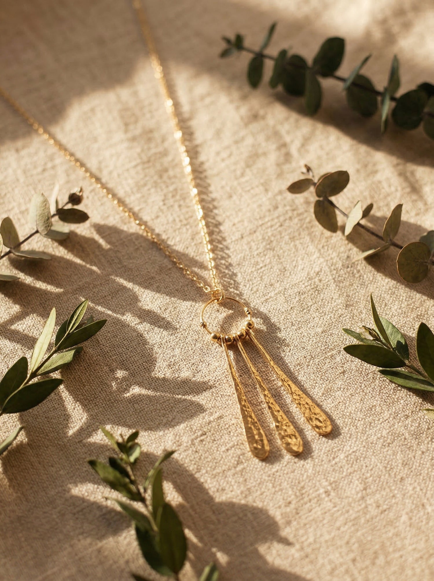 Gold necklace with tassel pendant on a textured surface with green leaves